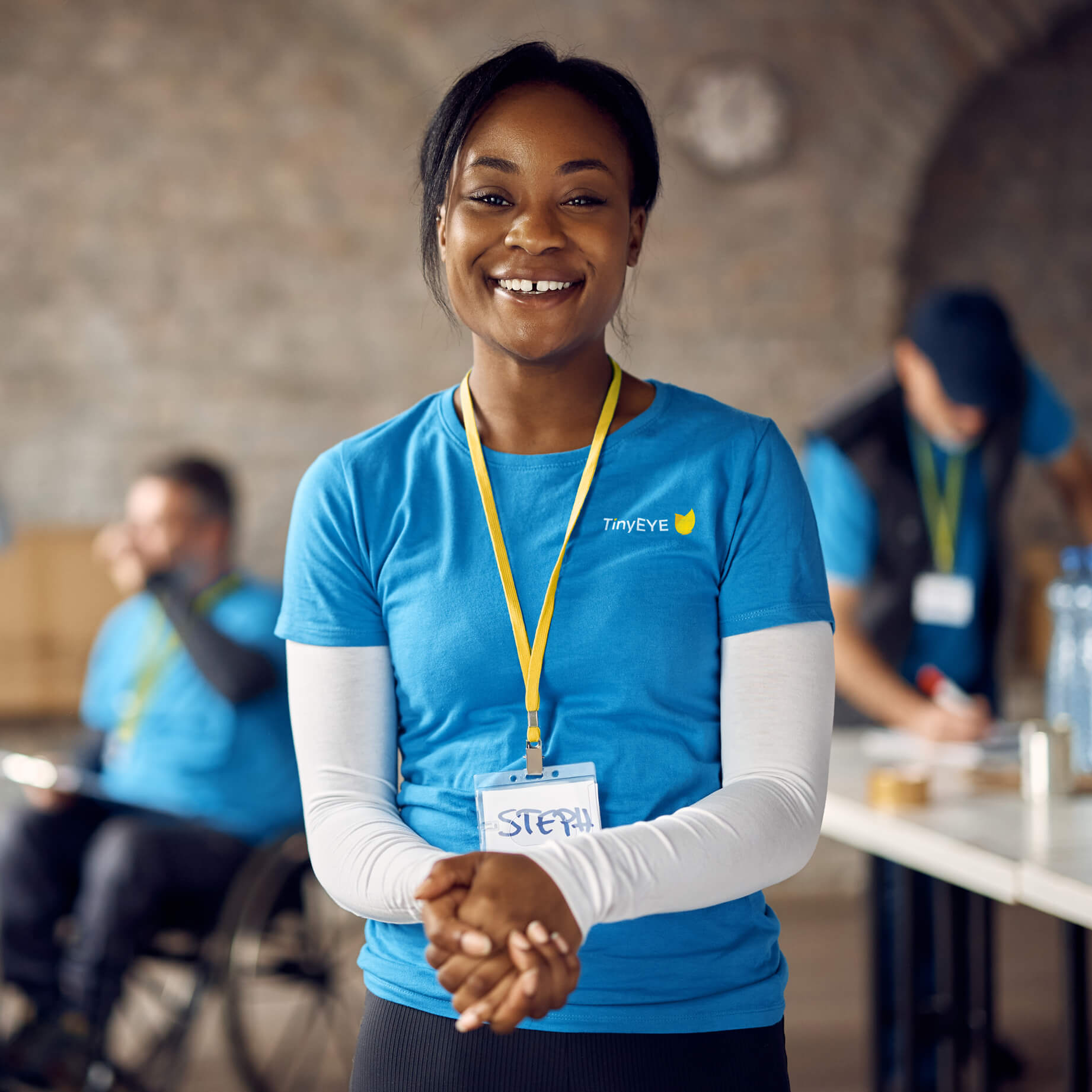 Smiling TinyEYE team member wearing a blue uniform and name badge, representing online therapy professionals in speech and occupational therapy.