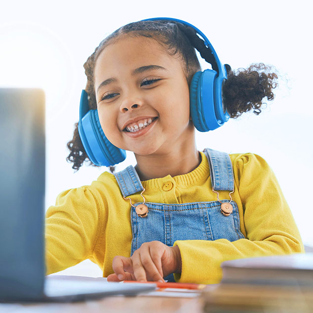 Smiling child wearing blue headphones and engaging in an online therapy session, representing TinyEYE speech and occupational therapy services.